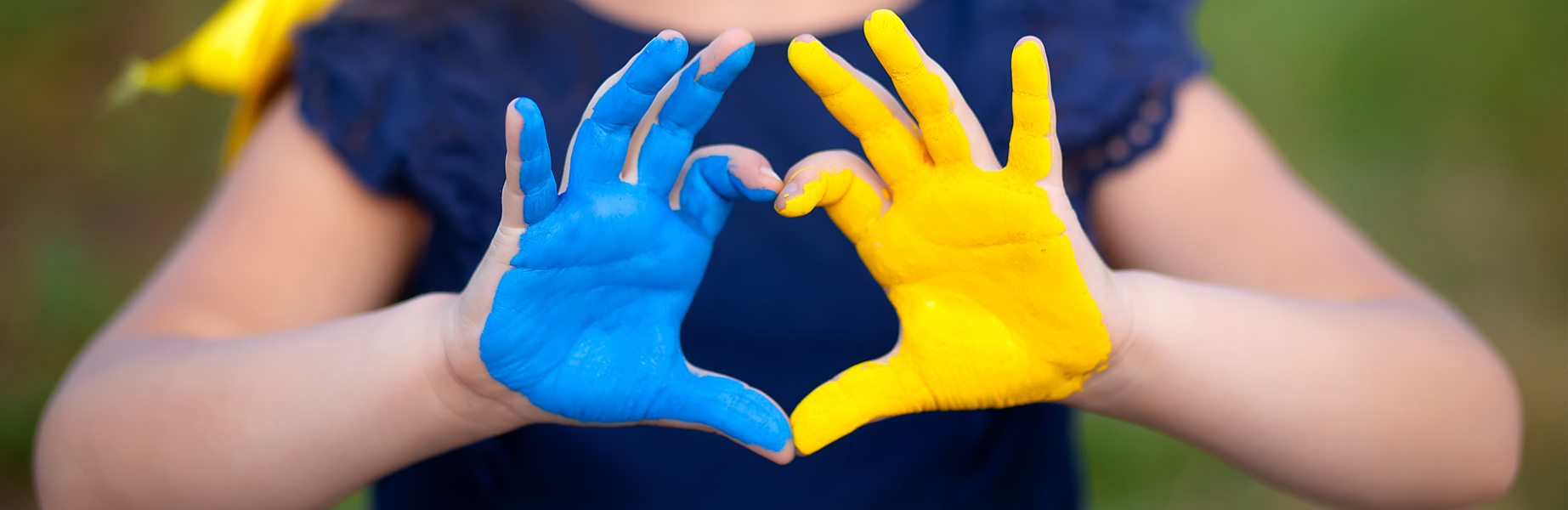 Kinderhände formen ein blau-gelbes Herz