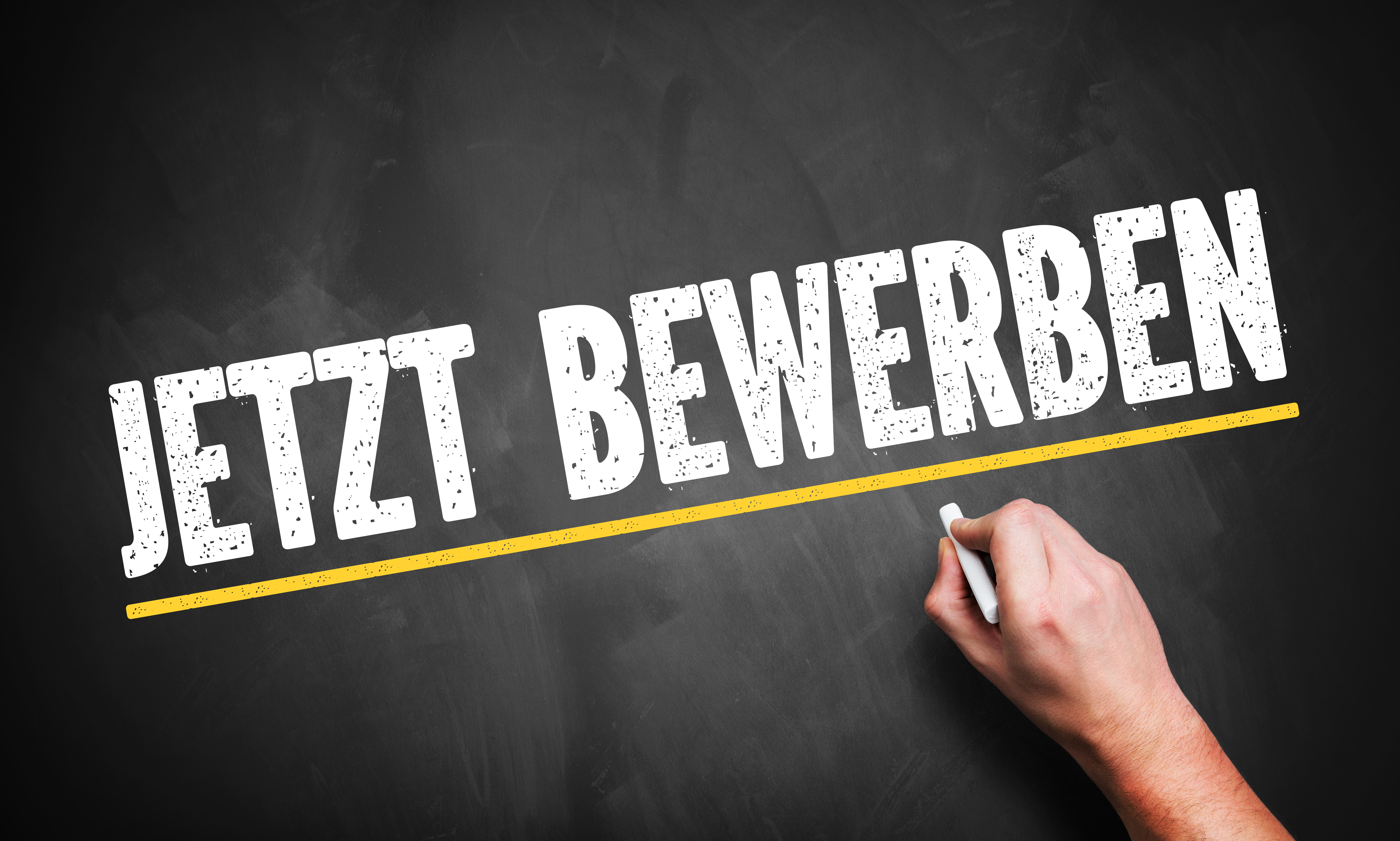 Eine Hand schreibt "Jetzt Bewerben" auf eine Tafel