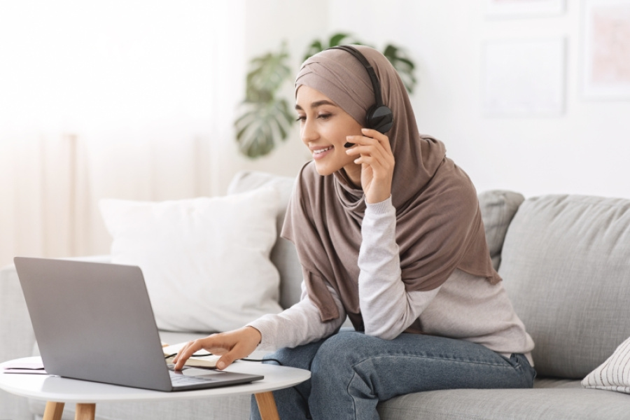 Frau mit Headset und Kopftuch am Laptop sitzend