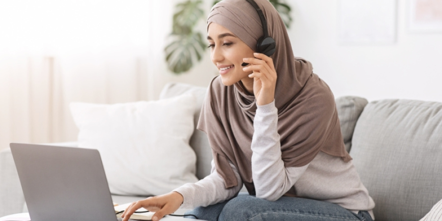 Frau mit Headset und Kopftuch am Laptop sitzend