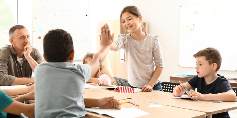 Schüler*innen an einem Tischen, die sich High Fiven