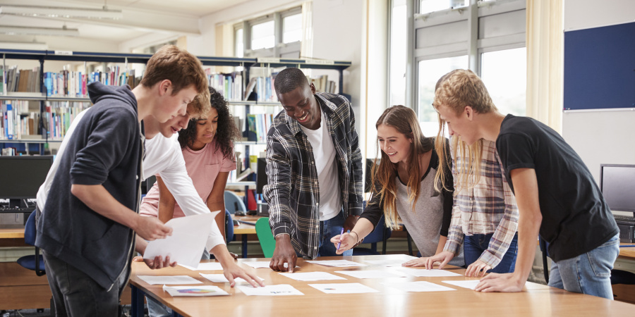 Eine Gruppe aus sieben Studenten stehen in einer Bibliothek um einen Tisch