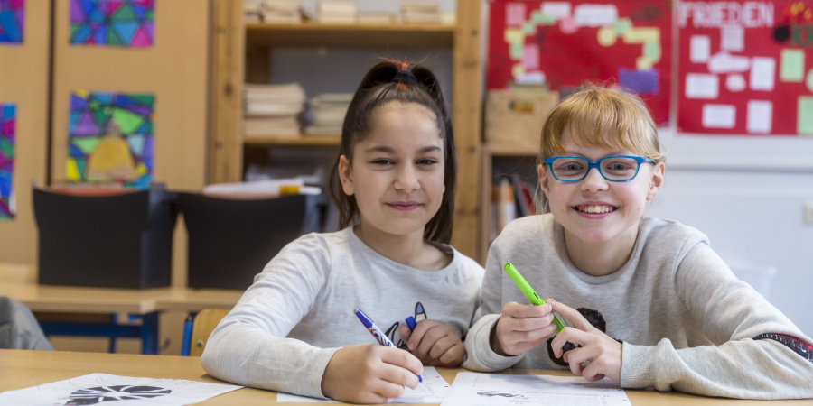 Zwei Mädchen arbeiten lachend gemeinsam an einem Arbeitsblatt