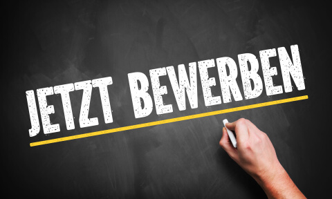 Eine Hand schreibt "Jetzt Bewerben" auf eine Tafel